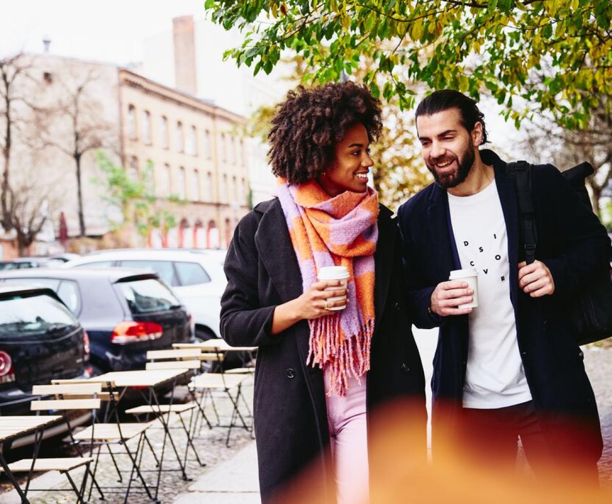 Smiling man and woman having a conversation while holding drinks and walking outside.