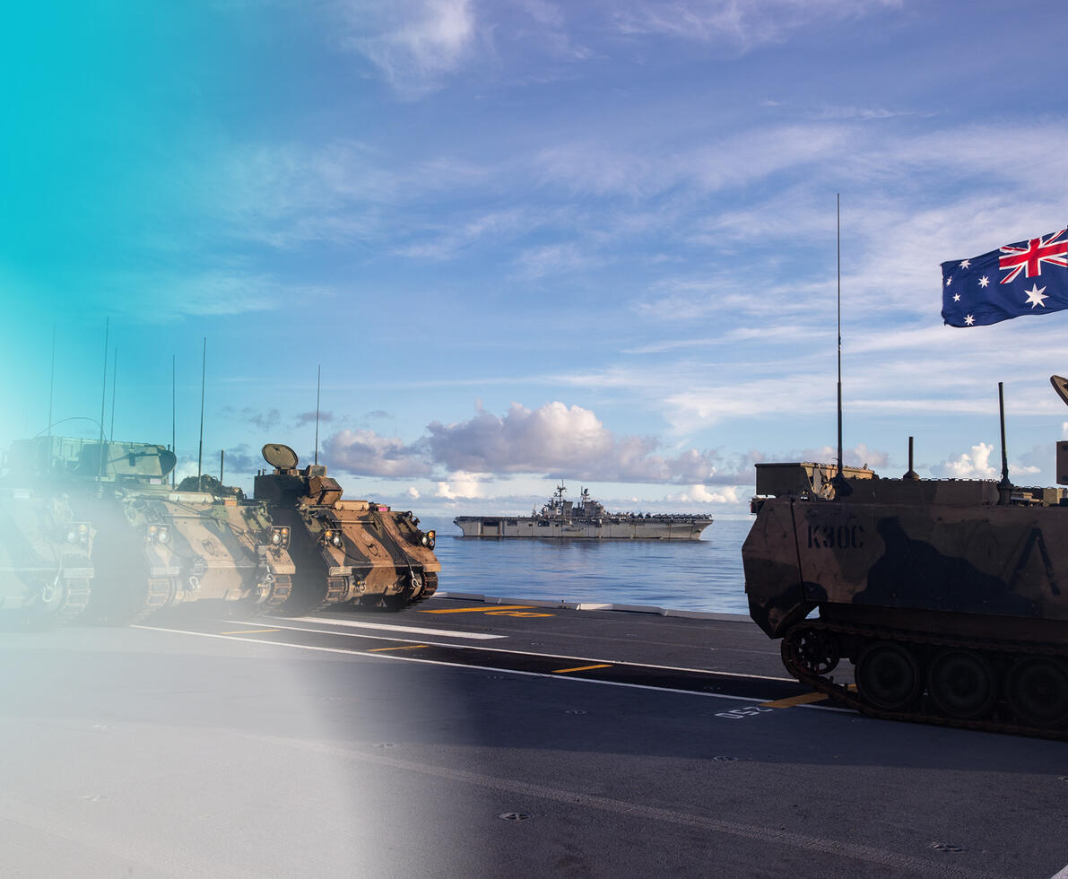 A photo of army tanks at a port with a naval ship from afar